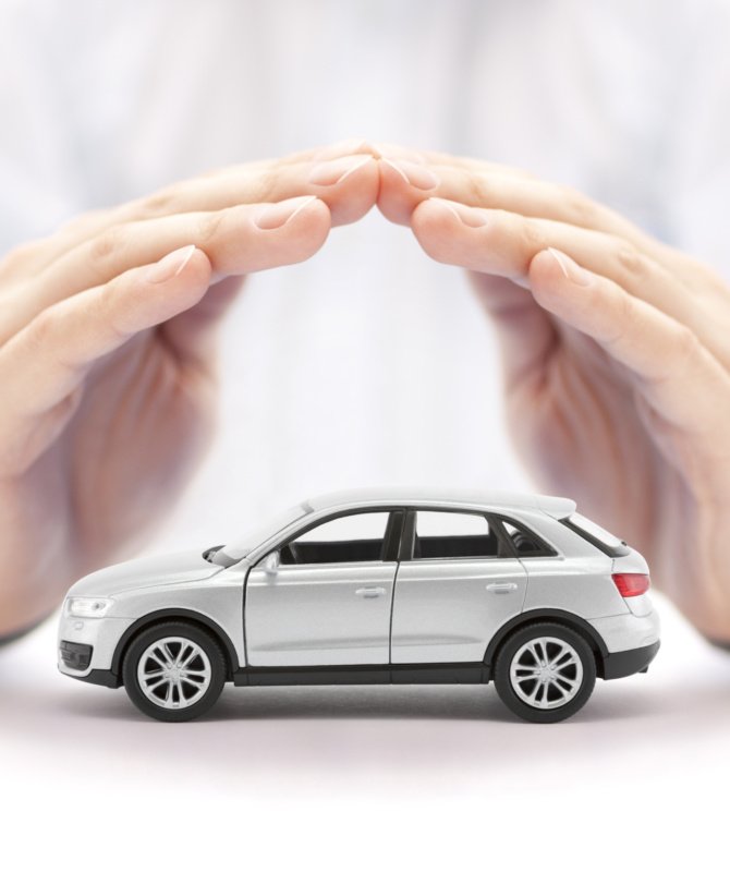 Car insurance. Small silver car covered by hands.